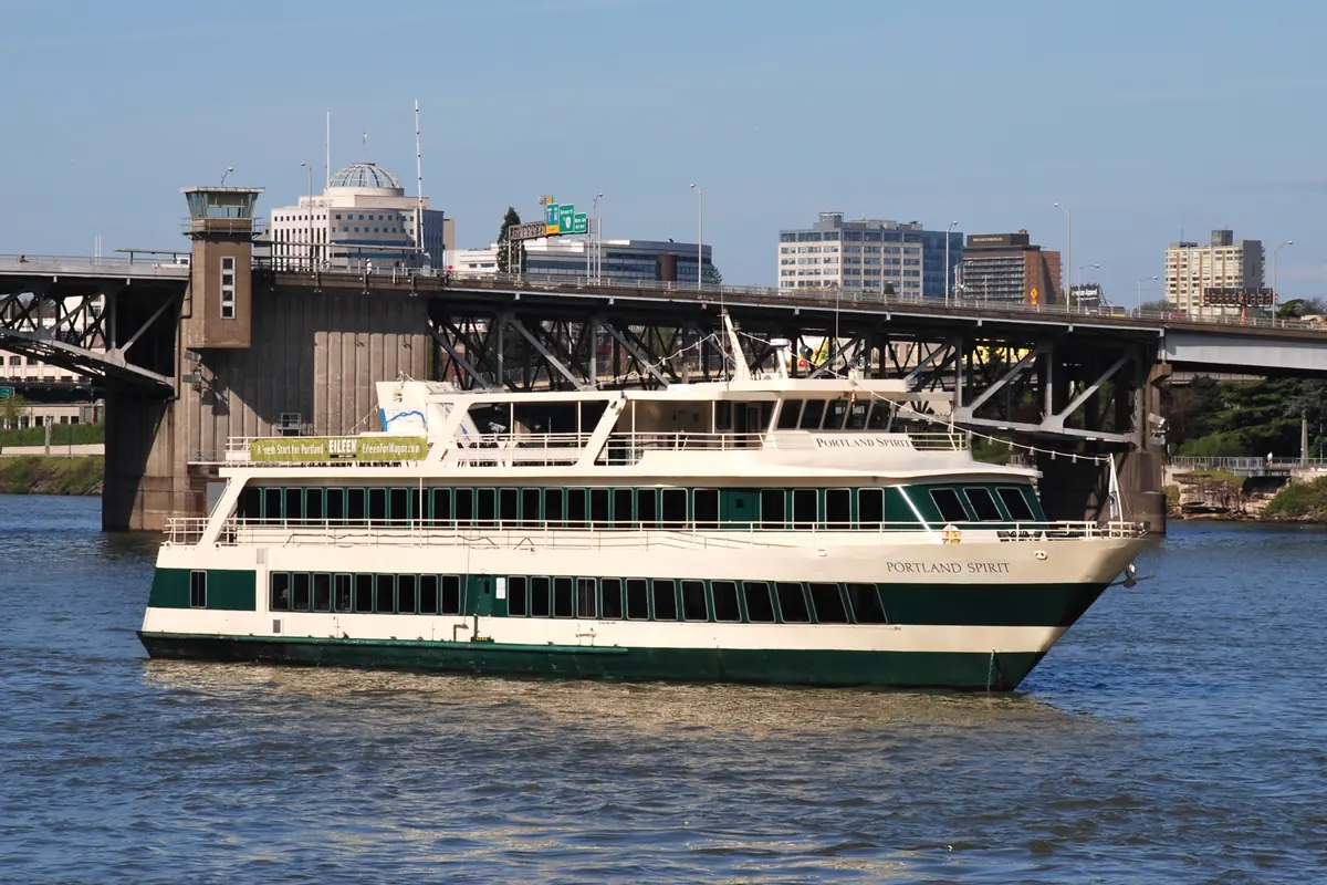 Um barco de cruzeiro Portland Spirit em tons de creme e verde no rio Willamette, em frente à Morrison Bridge