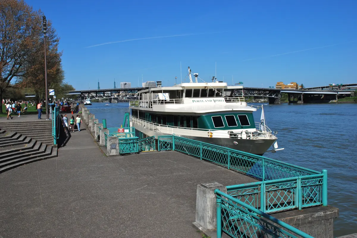 Pomost w Waterfront Park w centrum Portland, z betonowymi schodami, morską barierką i zacumowaną obok łodzią wycieczkową