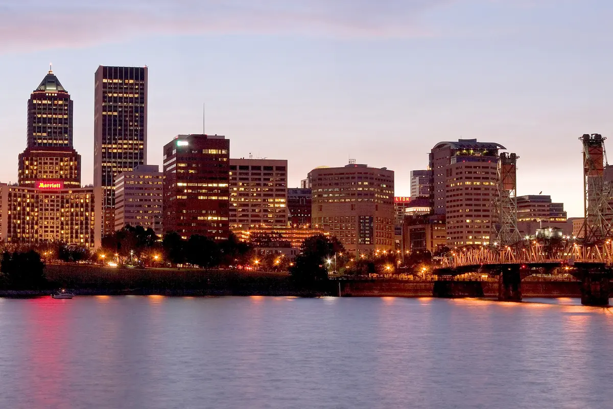 Wieżowce centrum Portland oświetlone o zmierzchu nad spokojną rzeką Willamette, z Hawthorne Bridge na prawym skraju