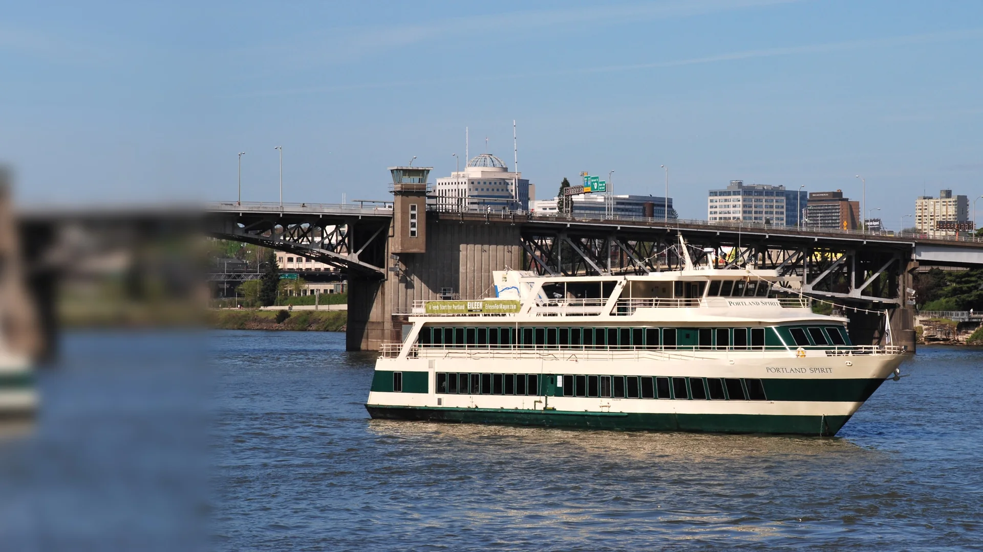 En cremefarvet og grøn middagsbåd fra Portland Spirit på Willamette River neden for Morrison Bridge i det centrale Portland