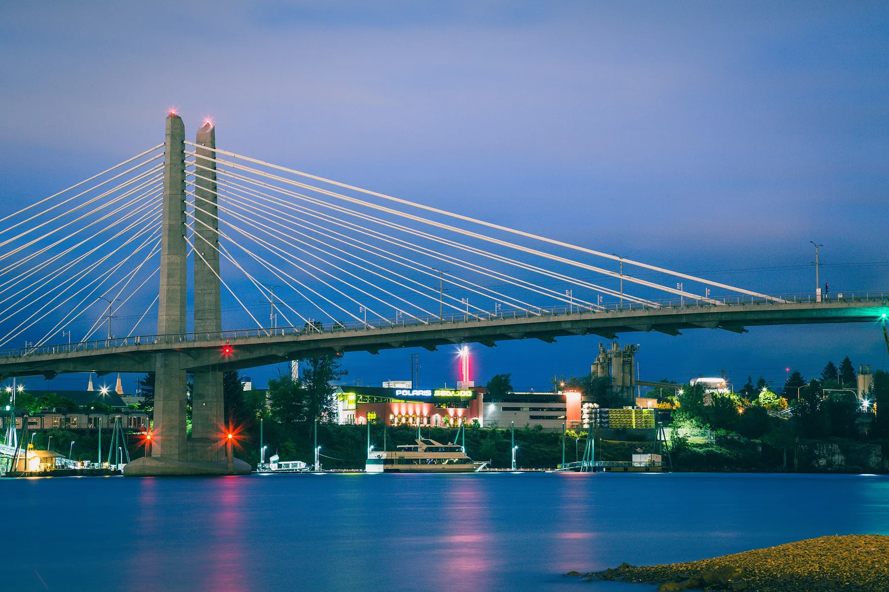 Tilikum Crossings hvide skråstagsmaster mod en blå-time-himmel, med en turistbåd fortøjet under spændet